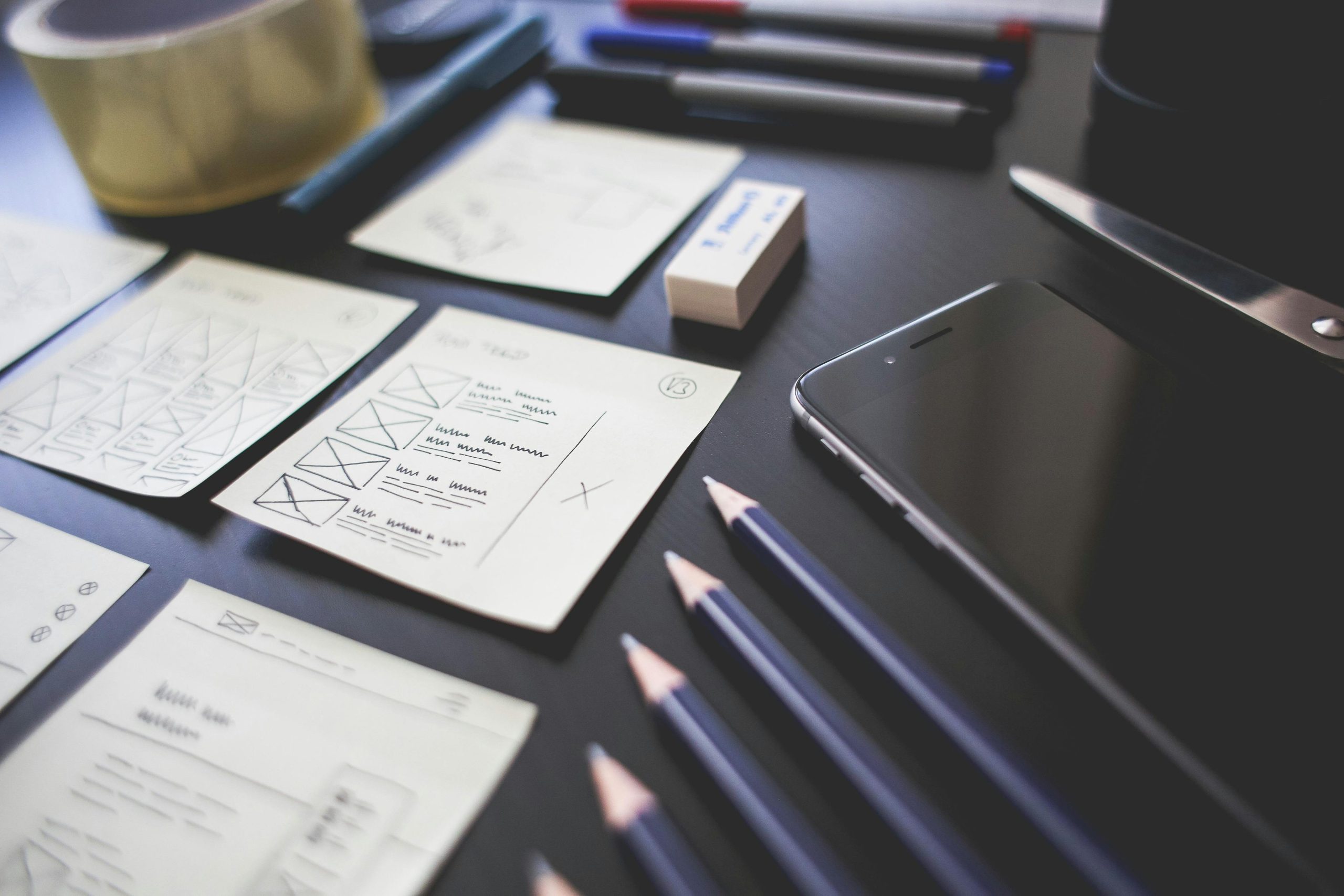 A creative workspace featuring UI design plans, pencils, a smartphone, and other office tools.